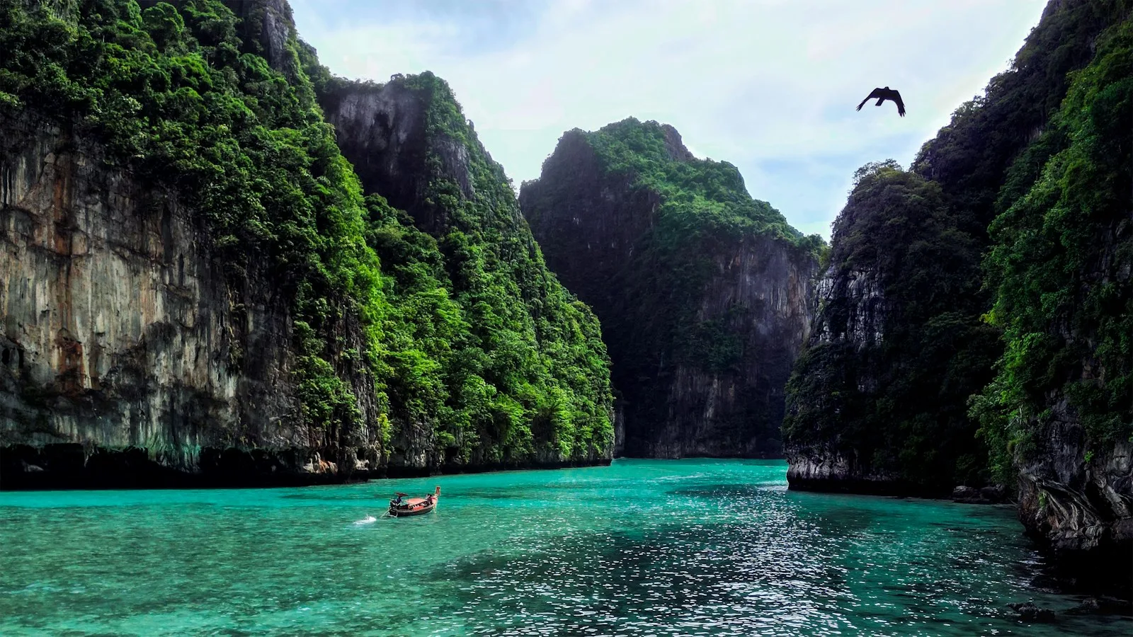 Bateau longtail sur des eaux turquoise au pied de falaises karstiques en Thaïlande